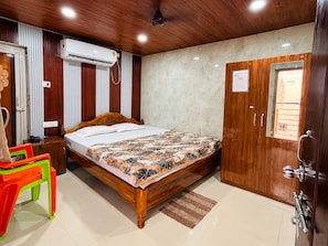 A hotel room with a wooden bed, a wardrobe, a desk, a chair, and an air conditioning unit. - Sabitri Guest House (Puri)