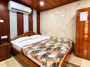 A hotel room with a wooden bed, a patterned bedspread, an air conditioning unit, a wardrobe, and a wall-mounted sign. - Sabitri Guest House (Puri)