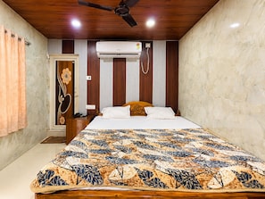 A bedroom with a bed, an air conditioning unit, a ceiling fan, and a door with a decorative handle. - Sabitri Guest House (Puri)