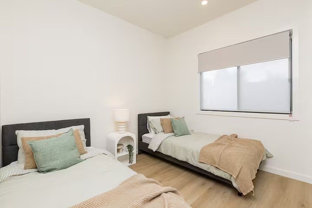 A bedroom with two beds, a window, and a bedside table with a lamp.