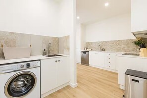 A modern kitchen with a built-in washing machine, a dishwasher, and a trash bin.