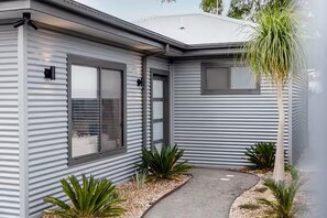 A modern house with a metal exterior, a front door, and a pathway leading to the entrance.