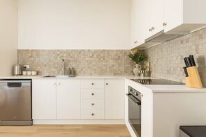 A modern kitchen with white cabinets, a dishwasher, a stove, and a tiled backsplash.