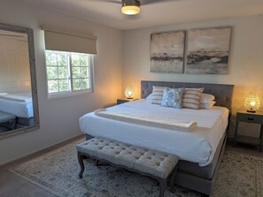 Ein Schlafzimmer mit einem großen Bett, zwei Nachttischlampen, einer Bank, einem Fenster und zwei Wandbildern.