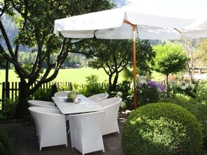 An outdoor patio with a table and chairs, a white umbrella, and a neatly trimmed hedge. - 1 in Katrin's House (Bad Hindelang)