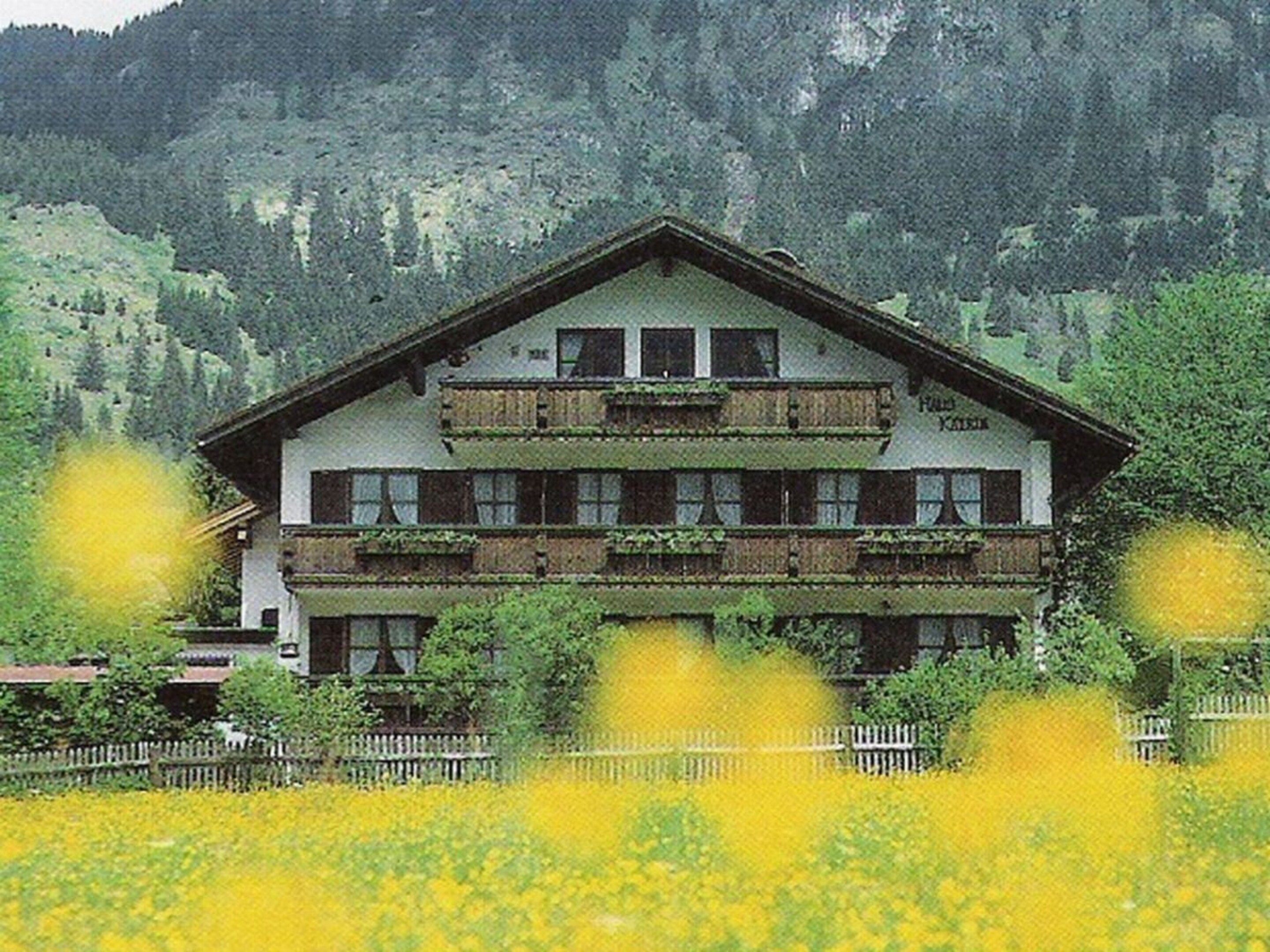 Un bâtiment à deux étages, doté d’un balcon à l’étage supérieur, entouré d’une clôture et d’un champ de fleurs jaunes.