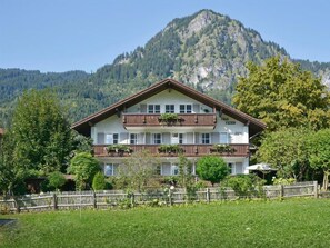 A two-story hotel with a balcony on the upper floor, surrounded by greenery and a mountain backdrop. - 1 in Katrin's House (Bad Hindelang)