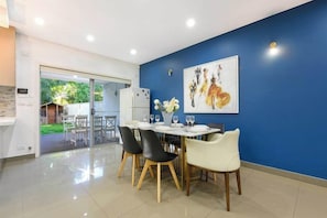 Uma sala de jantar com mesa posta para quatro pessoas, cadeiras e um vaso com flores.