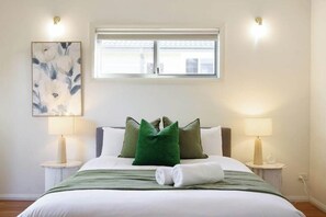 A hotel room with a bed, two bedside lamps, a window, and a wall-mounted artwork.