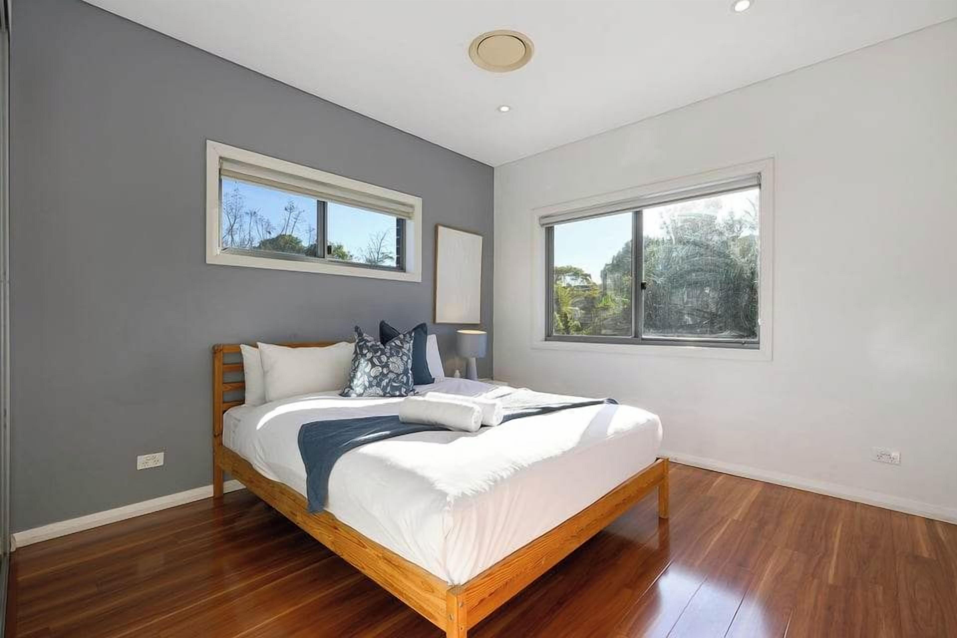 A bedroom with a wooden bed, two windows, and a ceiling light.