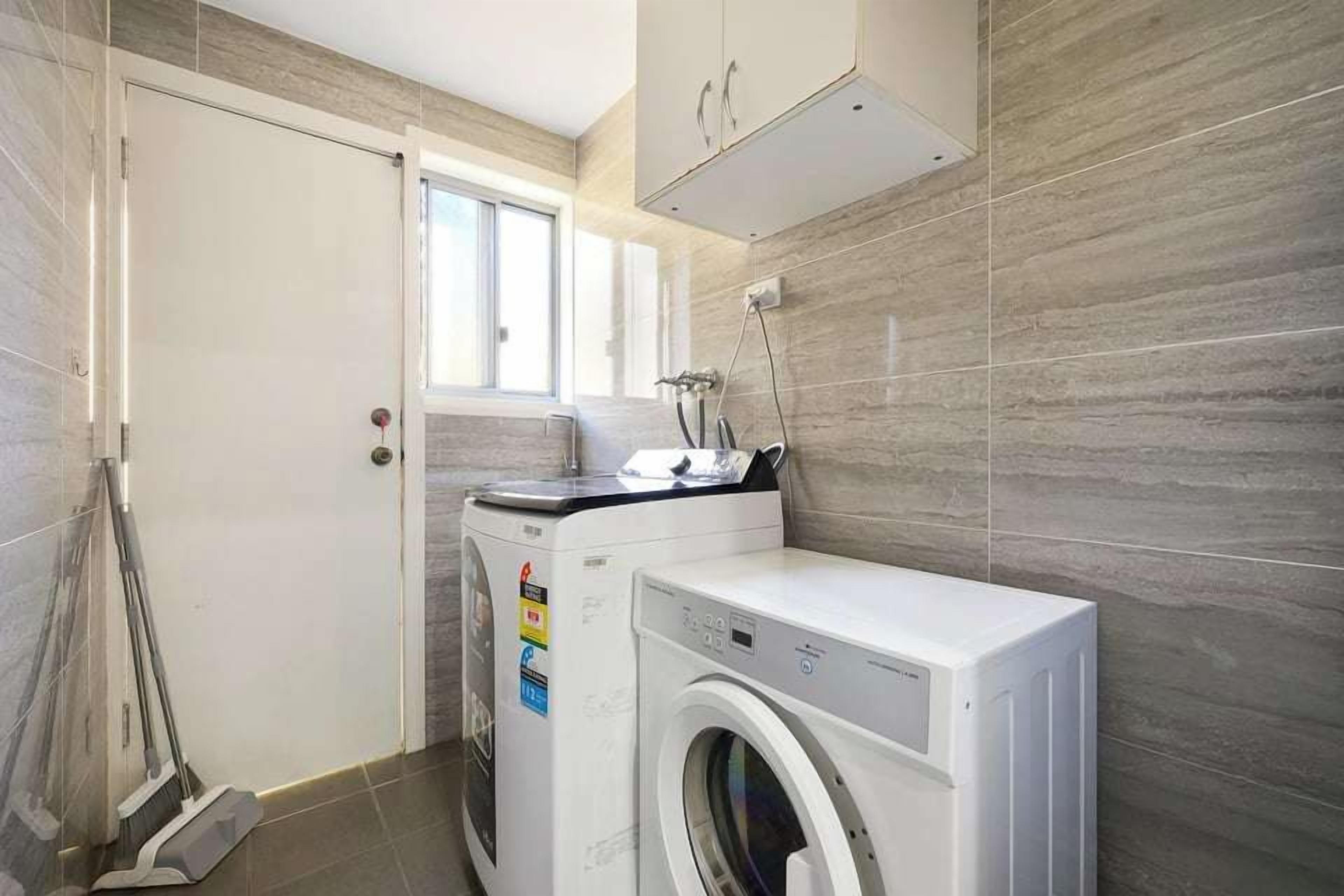 A compact laundry room with a washing machine, a drying rack, and a window providing natural light.
