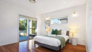 A modern bedroom with a large bed, a sliding glass door leading to a balcony, and a small table with a lamp. - Spacious 5BR Home Near Westmead and Parramatta (Northmead)