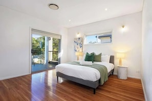 Quarto moderno com uma cama grande, uma porta de vidro deslizante que dá para uma varanda e uma mesinha de cabeceira com abajur.