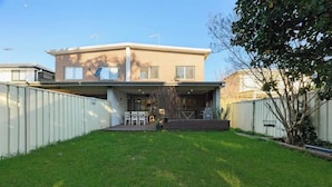 A two-story house with a flat roof, a covered patio, and a fenced backyard. - Spacious 5BR Home Near Westmead and Parramatta (Northmead)