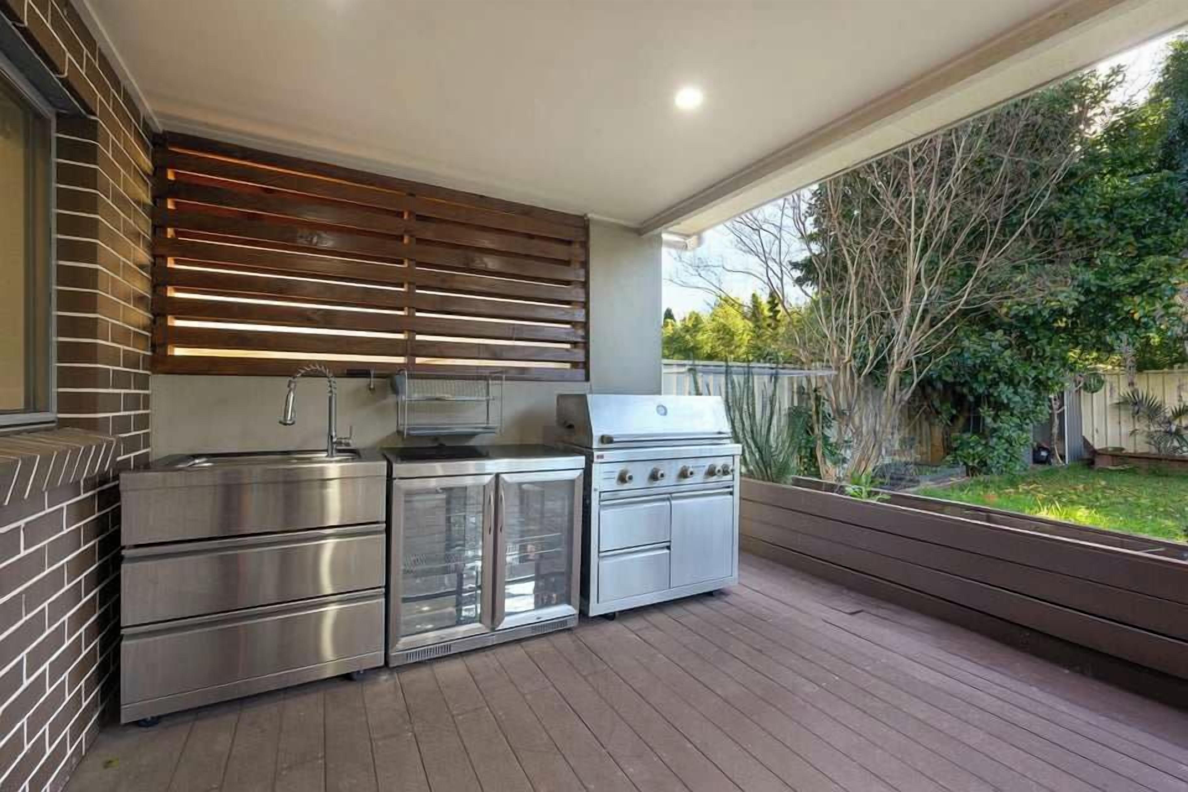 An outdoor kitchen with stainless steel appliances, a brick wall, and a wooden deck.