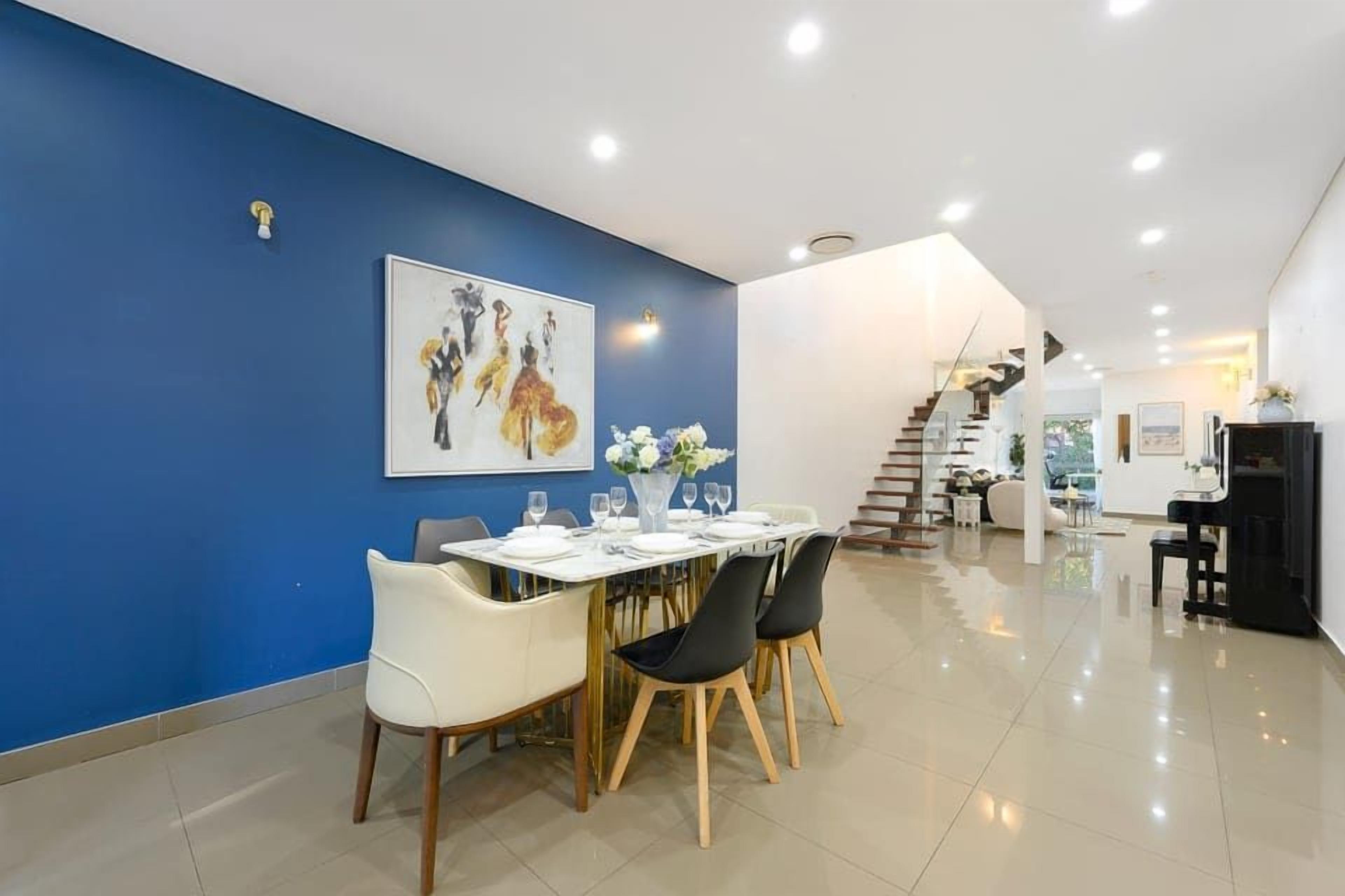 A modern dining area with a blue accent wall, a dining table set for four, and a staircase leading to an upper level.