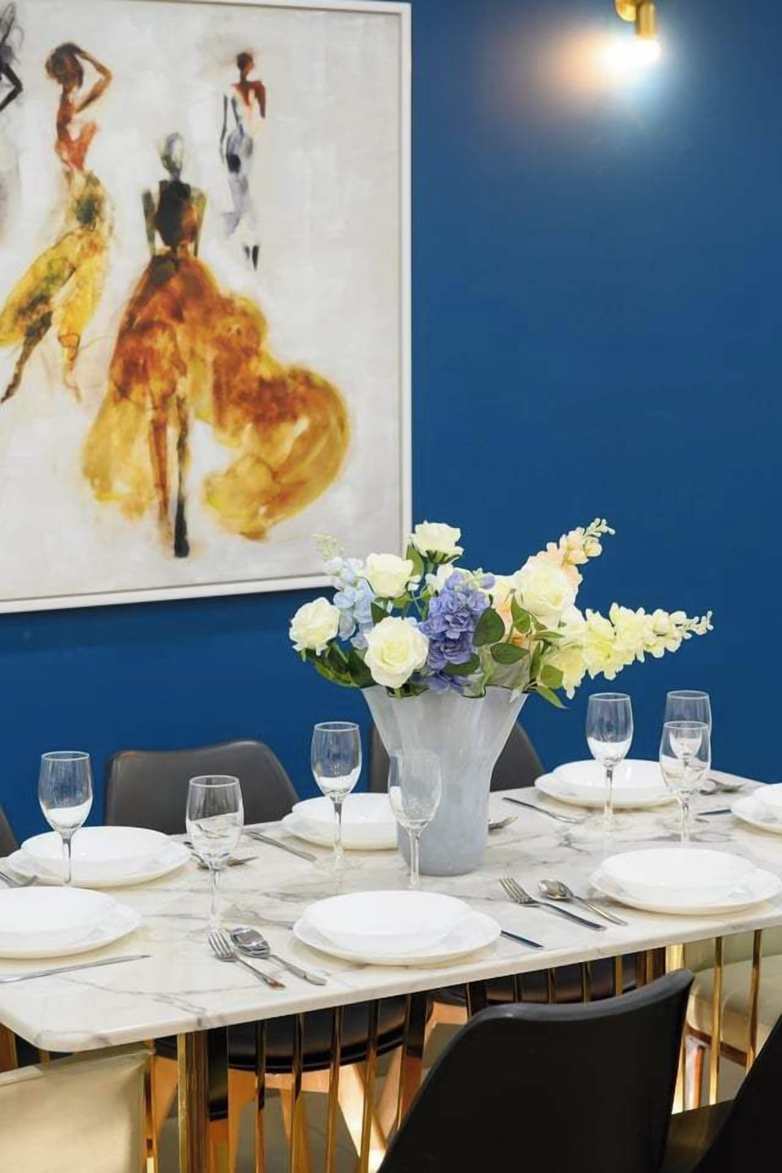 A dining table set with plates, glasses, and cutlery, a vase with flowers, and a painting on the wall.