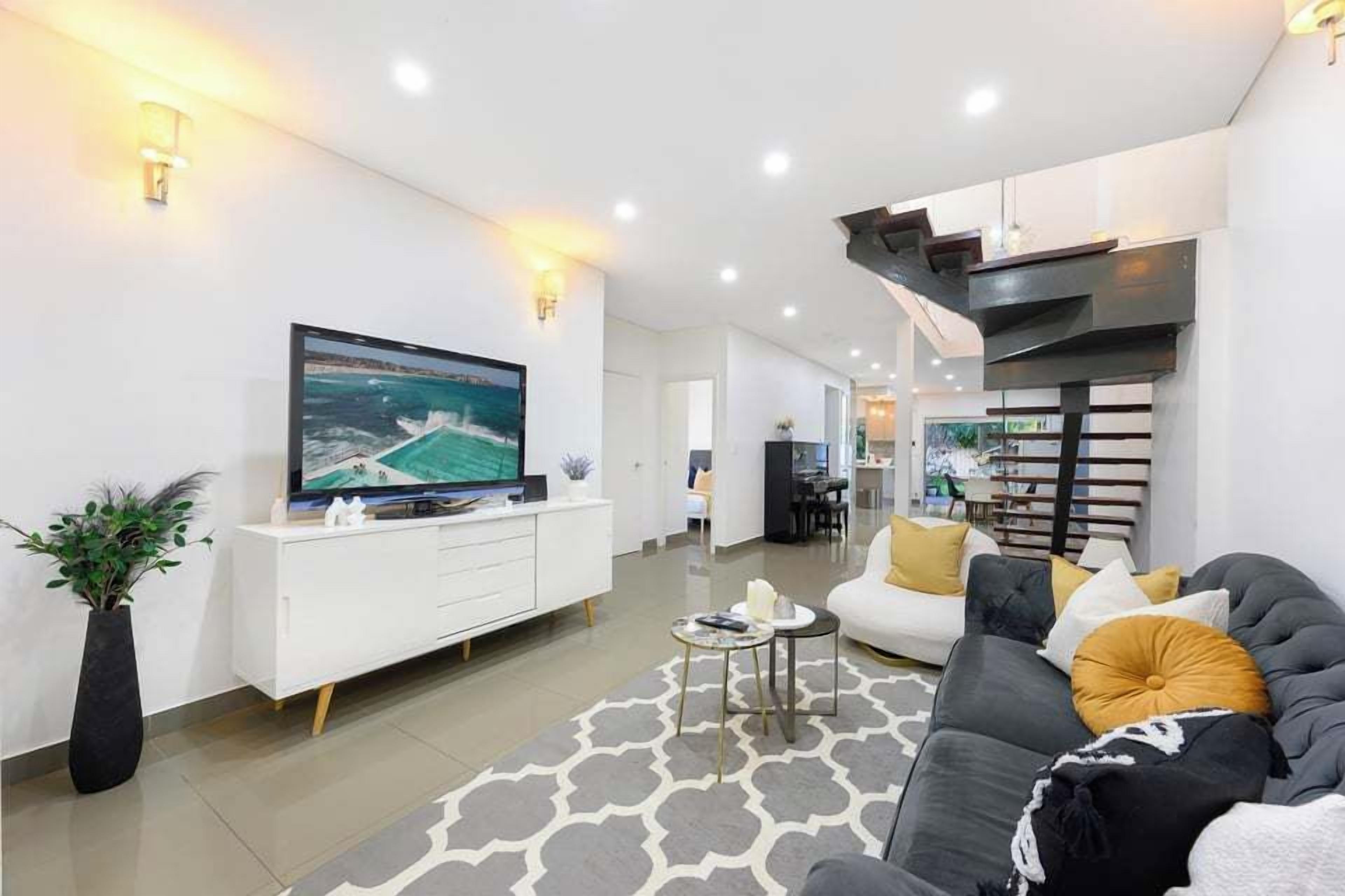 A modern living room with a flat-screen TV, a sofa, a coffee table, and a decorative rug.