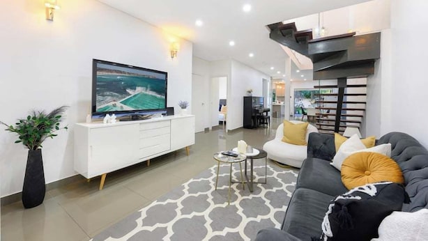 A modern living room with a flat-screen TV, a sofa, a coffee table, and a decorative rug. - Spacious 5BR Home Near Westmead and Parramatta (Northmead)
