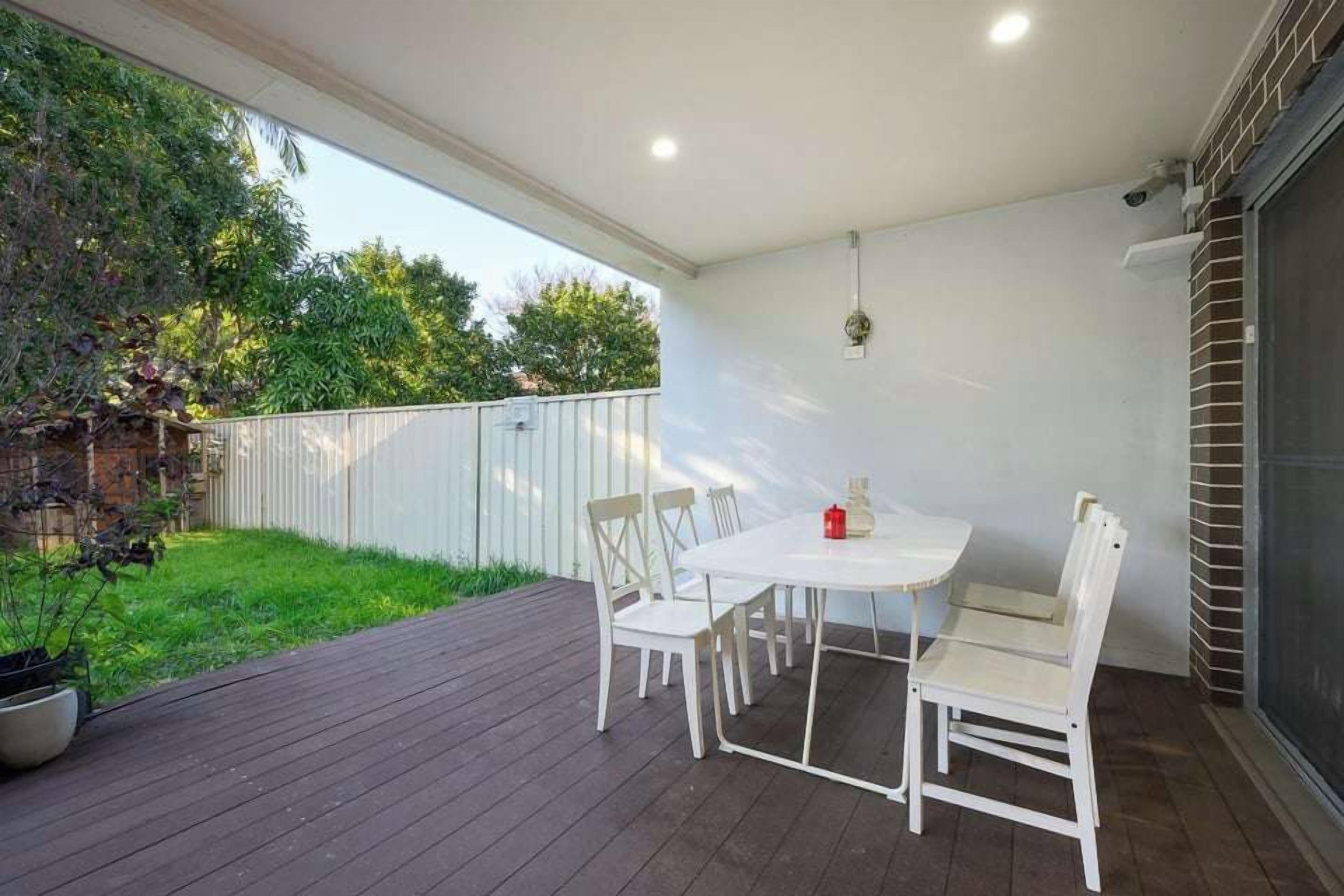 An outdoor patio with a white table and chairs, surrounded by a wooden deck and a white fence.