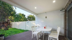 An outdoor patio with a white table and chairs, surrounded by a wooden deck and a white fence. - Spacious 5BR Home Near Westmead and Parramatta (Northmead)