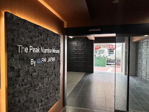 A reception area with a stone wall and a sign reading 'The Peak Namba Minami By FM JAPAN'. - The Peak Namba Minami (Shikitsuhigashi, Naniwa Ward)