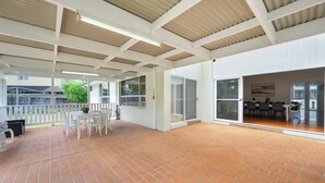Ein überdachter Patio-Bereich mit Backsteinboden, weißen Möbeln und Blick ins Freie.