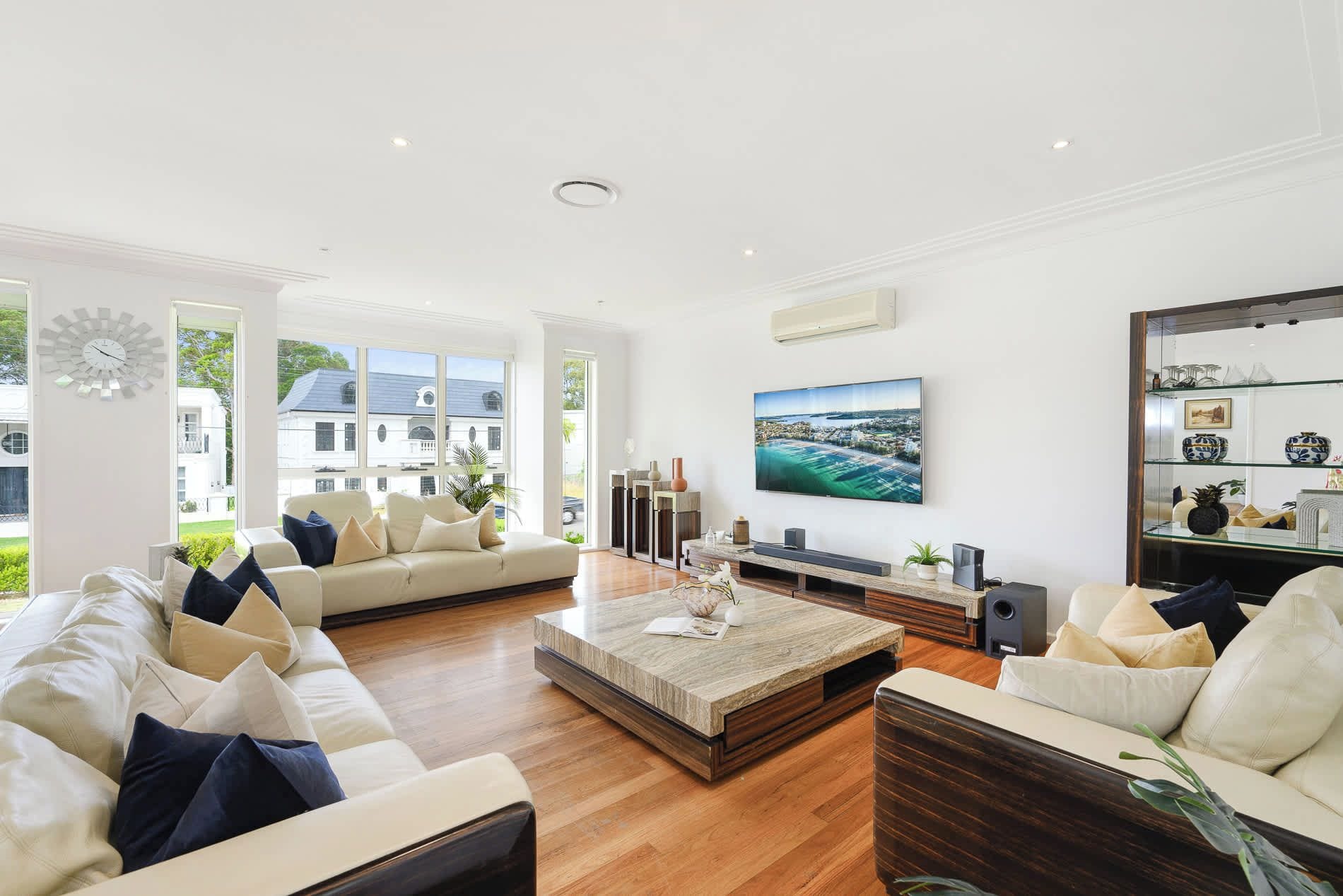 A spacious living room with a large flat-screen TV, comfortable seating, and a view of a white building outside.