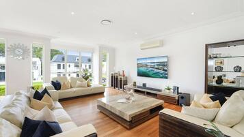 A spacious living room with a large flat-screen TV, comfortable seating, and a view of a white building outside.