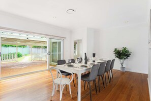 A dining area with a white table set for six, surrounded by grey chairs, and a potted plant on the right. - Vintage 5BR Retreat in Oatlands (Oatlands)