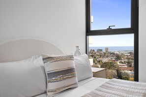 A bed with white bedding and a view of a cityscape through a window. - Sky-view 2-bed Apartment Near St Kilda Beach (Melbourne)