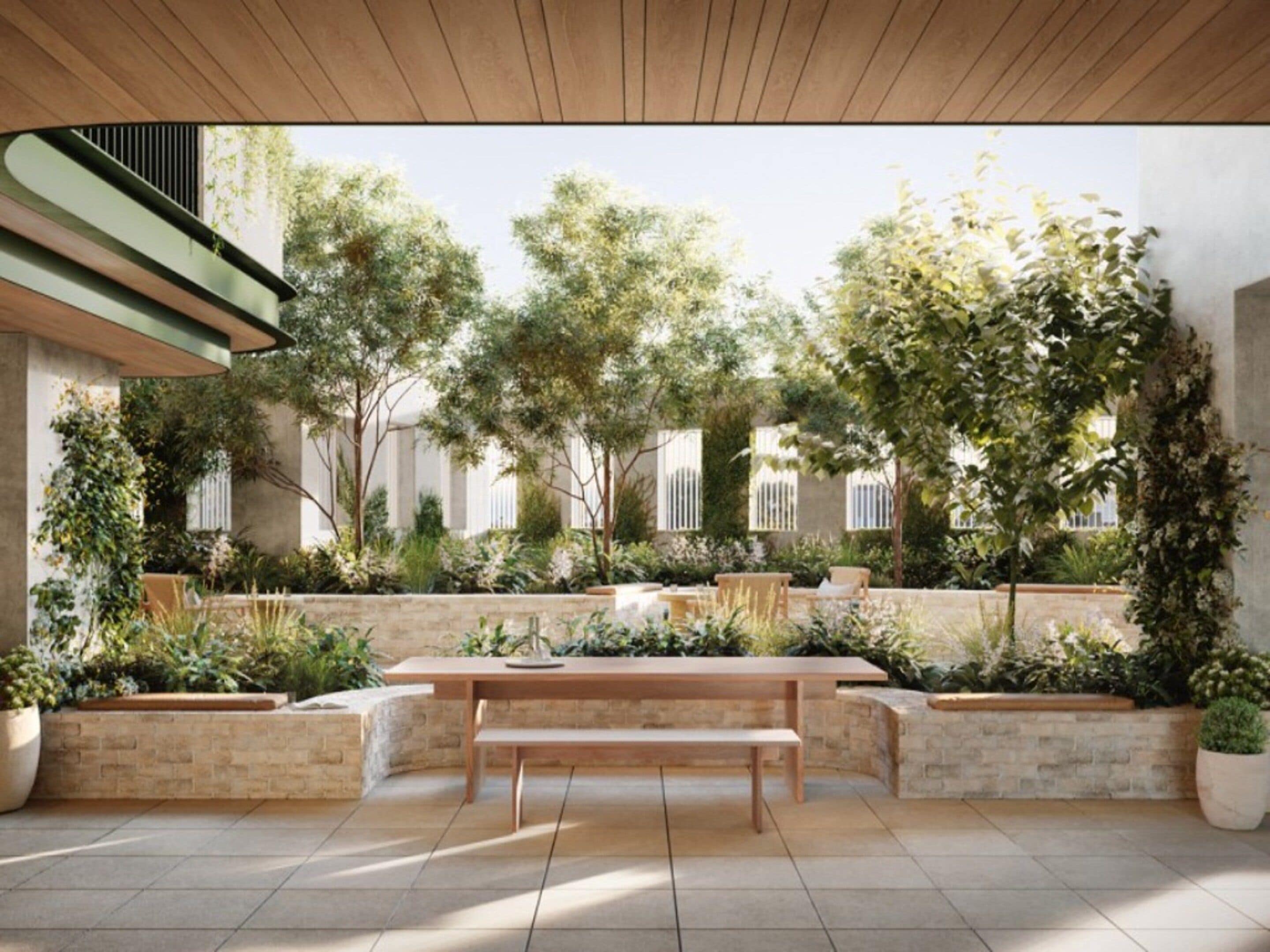 An outdoor patio with a wooden table and benches, surrounded by potted plants and trees.