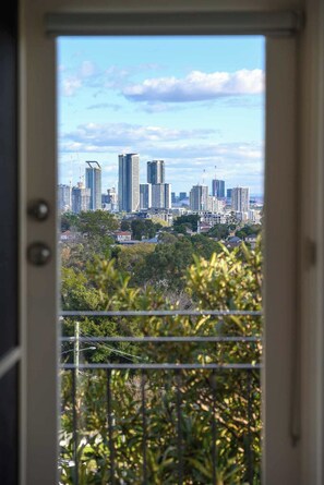 A view through a door of a cityscape with high-rise buildings and greenery. - Modern 2BR Apt Near Eastwood, Top Ryde and Transport (Ryde)