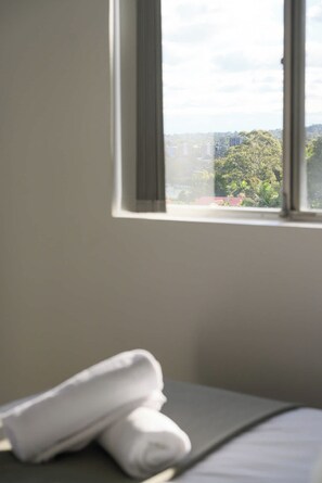 A room with a bed, a window, and a view of buildings and trees outside. - Modern 2BR Apt Near Eastwood, Top Ryde and Transport (Ryde)
