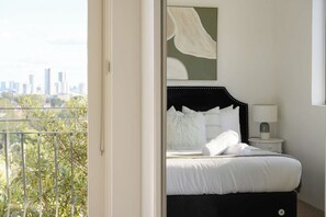 A bedroom with a bed, a bedside lamp, and a view of a cityscape through a balcony. - Modern 2BR Apt Near Eastwood, Top Ryde and Transport (Ryde)