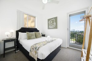 A bedroom with a bed, bedside table, lamp, and a view of the city through a balcony. - Modern 2BR Apt Near Eastwood, Top Ryde and Transport (Ryde)