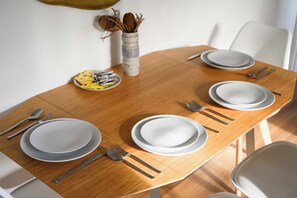 Mesa de jantar posta com pratos, talheres e uma tigela de frutas.