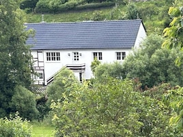 A white building with a dark roof, surrounded by dense greenery.