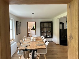 A dining area with a wooden table, white chairs, a chandelier, and a black cabinet with glass doors.