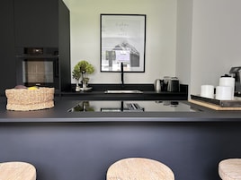 A modern kitchen with a black countertop, a framed picture on the wall, and a basket of fruits.