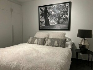 A bedroom with a white fluffy bed, two pillows with tree patterns, a framed black and white photograph on the wall, and a lamp on a side table. - Romantic Cabin Winterberg-willingen (Medebach)
