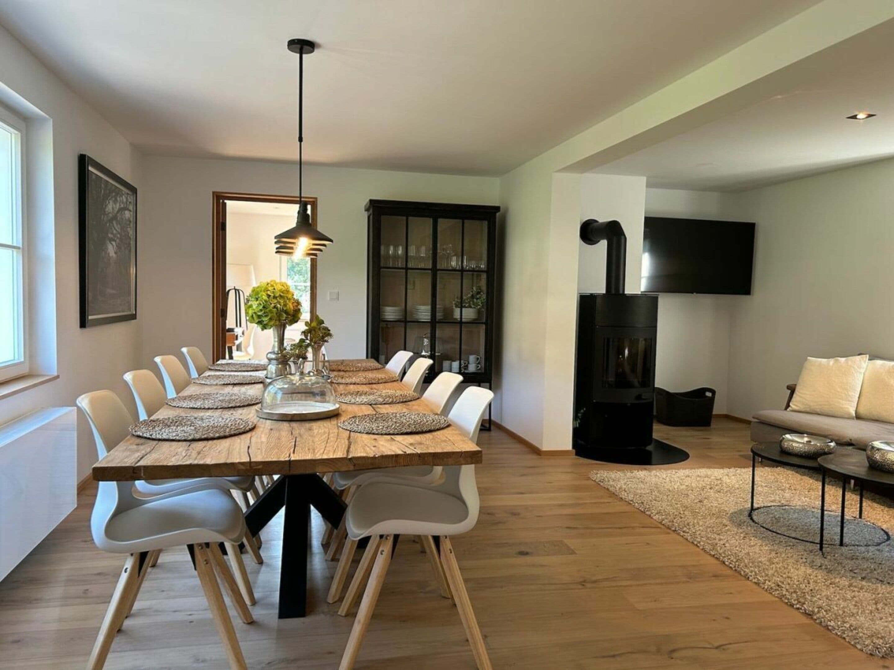 A dining area with a long wooden table, white chairs, and a modern pendant light.