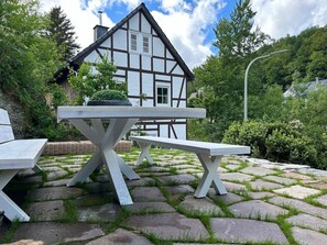 Ein traditionelles Fachwerkhäuschen mit einer Steinterrasse und Sitzgelegenheiten im Freien.