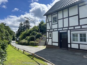 Ein traditionelles Fachwerkhäuschen mit einer Haustür, einer Treppe, die zum Eingang führt, und einem gepflasterten Zugangsbereich.