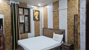 A hotel room with a bed, a nightstand, a wall-mounted shelf, and a window with a curtain. - The Viyan Vrindavan (Dhorera Khadar)