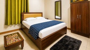 A hotel room with a bed, a wooden wardrobe, a small table with a floral tablecloth, and a painting on the wall. - The Viyan Vrindavan (Dhorera Khadar)