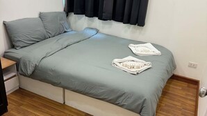 Un lit simple avec un matelas et des oreillers gris, un plancher en bois et une fenêtre avec des rideaux foncés.