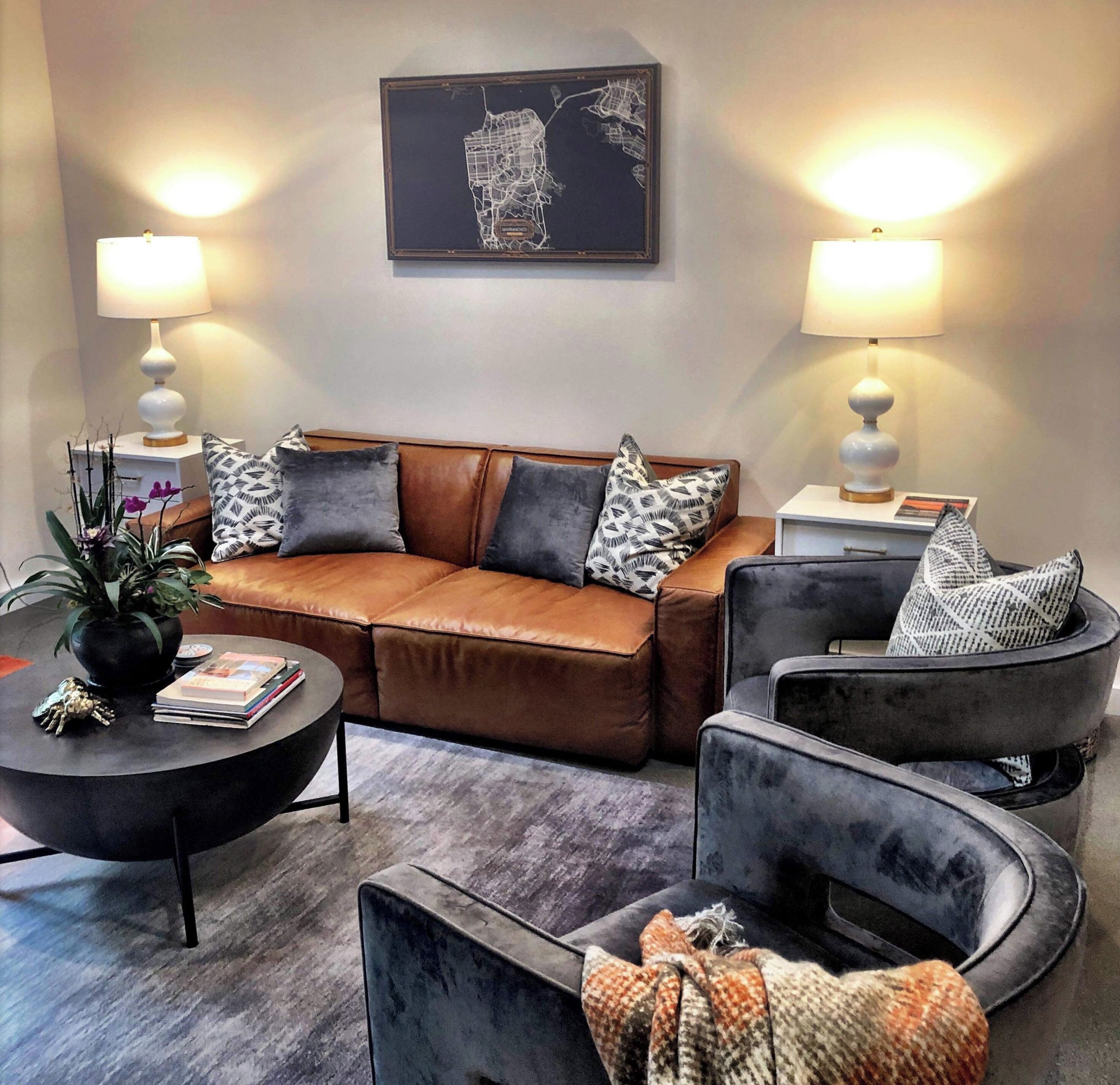 A modern living room with a brown leather sofa, two armchairs, a coffee table, and a wall-mounted abstract artwork.