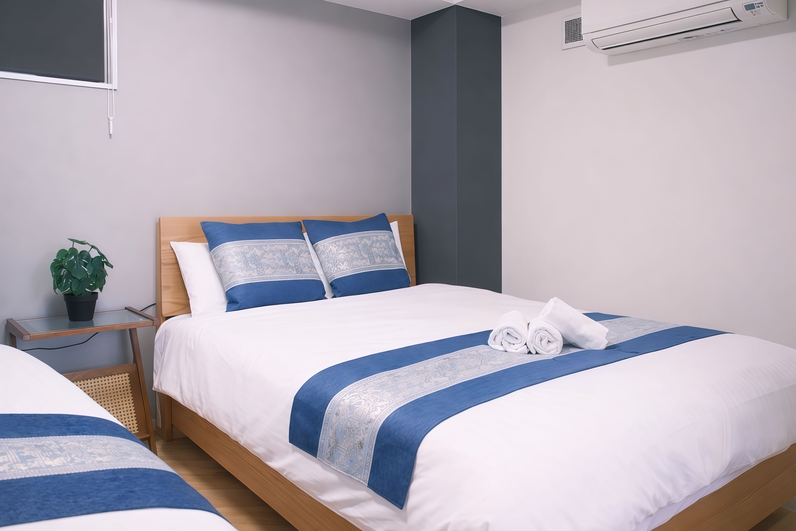 A hotel room with a bed, a nightstand, a potted plant, and an air conditioning unit.