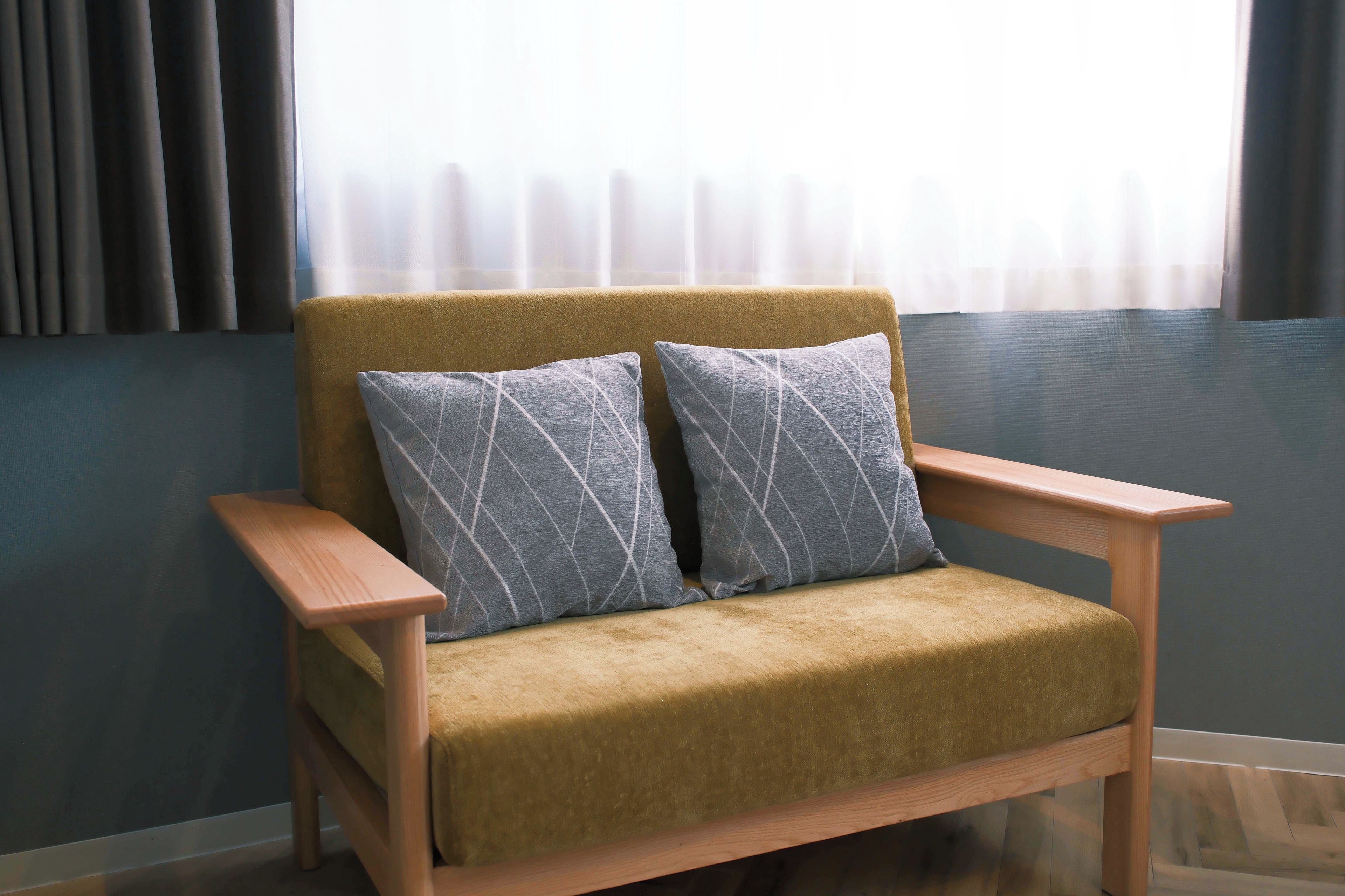 A chair with a cushion and a wooden armrest, positioned in a room with a window and curtains.